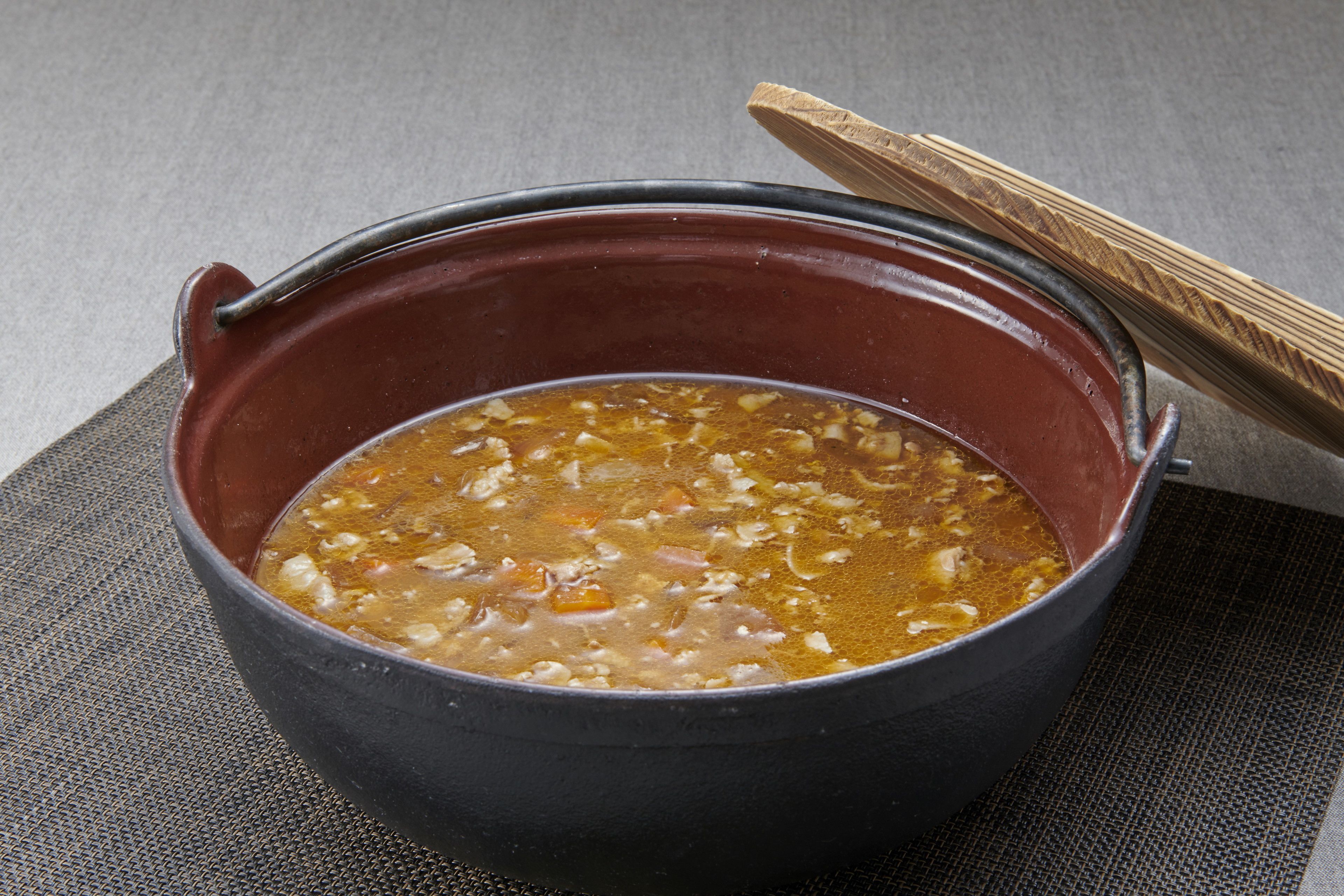 A pot of soup with a wooden spoon on a textured mat.