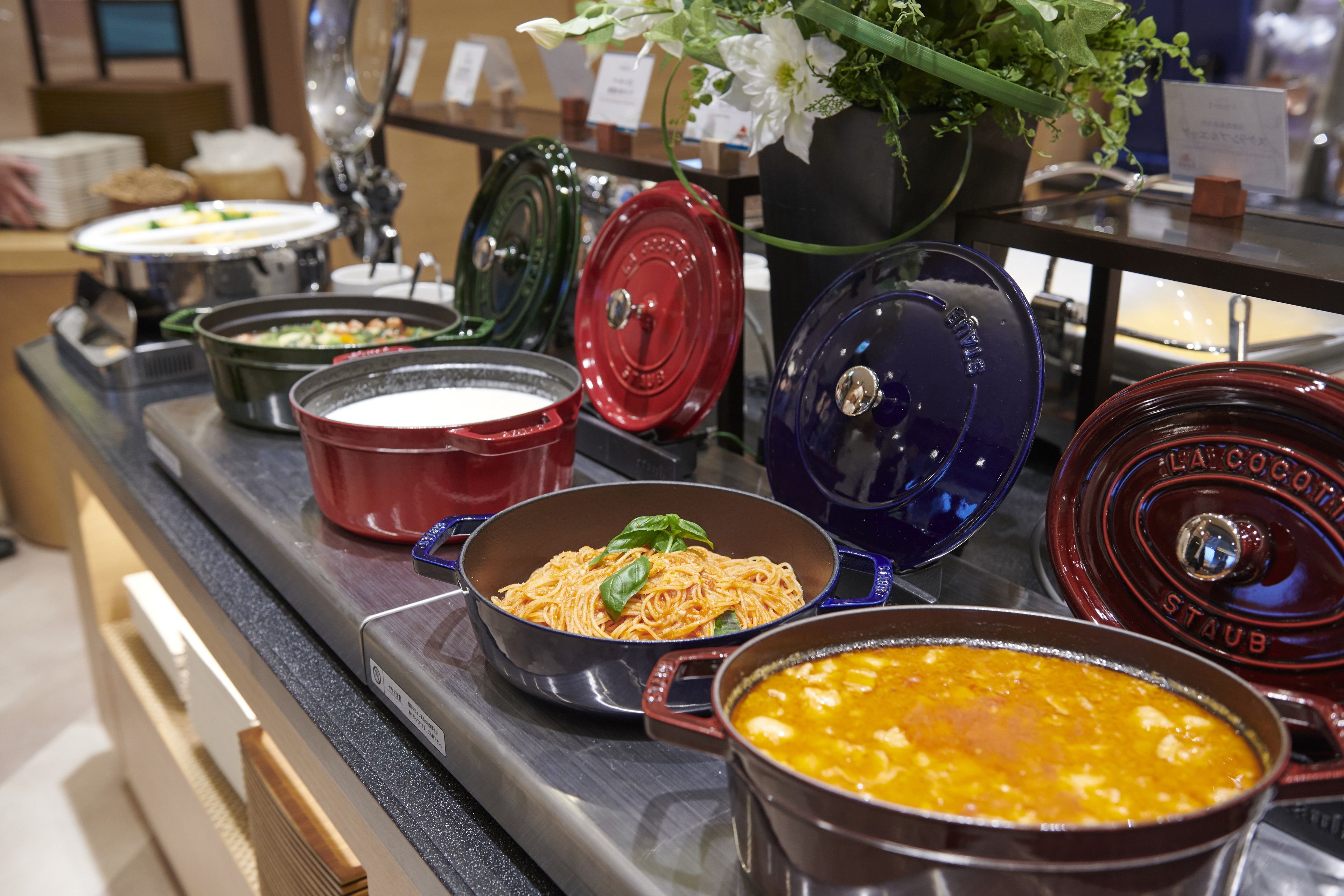 A buffet with various dishes in different colored pots and bowls.