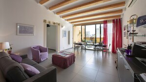 A living room with a sofa, armchair, and ottoman, a dining area with chairs and a table, and a kitchen area with a coffee machine. - Bed & Breakfast Terrazze Villanova (Trapani)