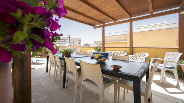 An outdoor patio with a wooden ceiling, a table with chairs, and a view of buildings in the background. - Bed & Breakfast Terrazze Villanova (Trapani)