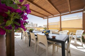 Eine Terrassengaststätte mit Holzboden, einem Tisch mit Stühlen und Blick auf Gebäude im Hintergrund.