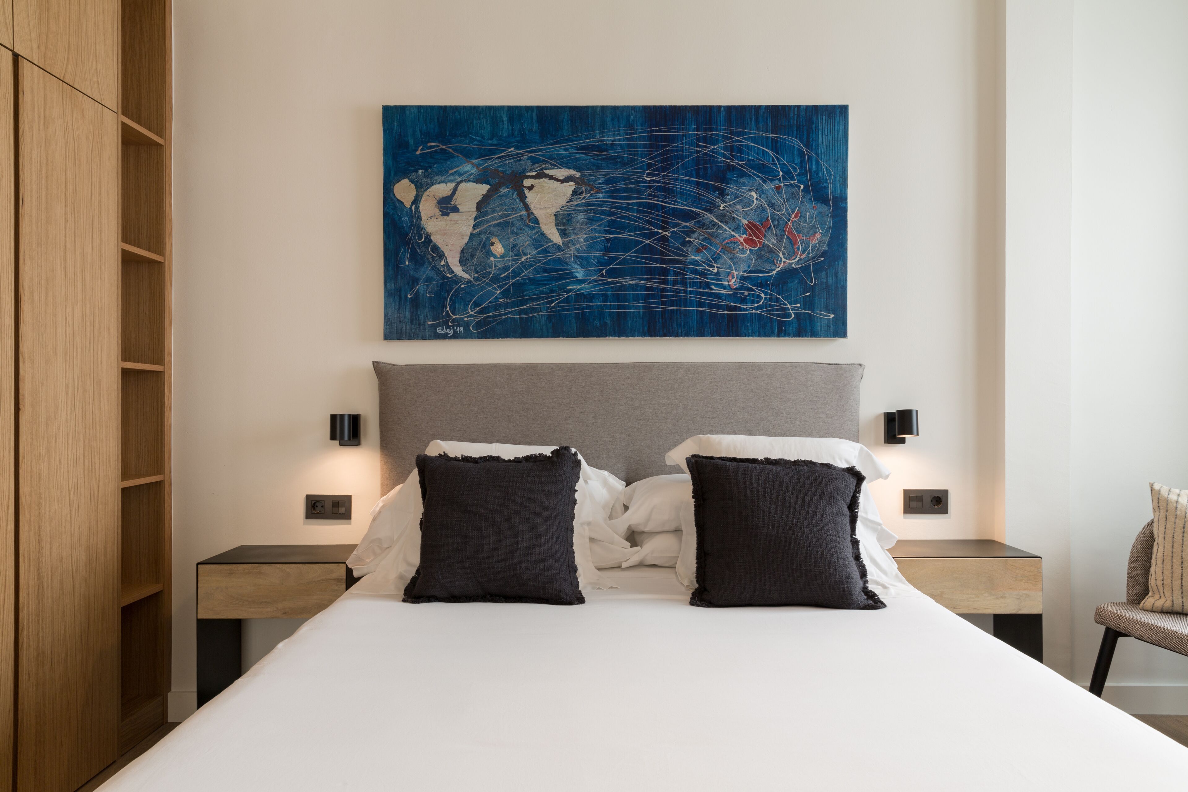 A modern bedroom with a large bed, two bedside tables, a wooden wardrobe, and a world map artwork on the wall.