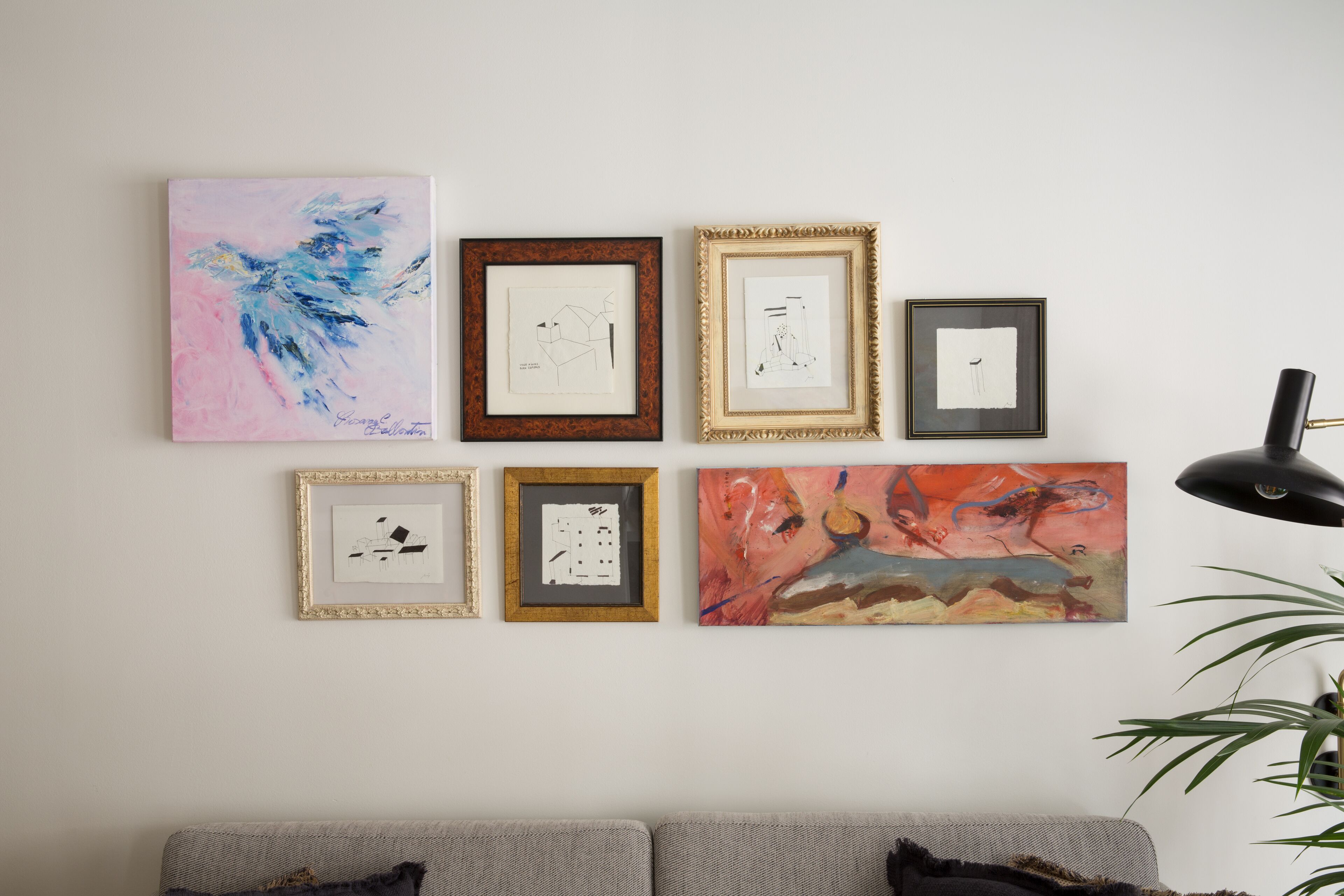 A wall with eight framed artworks of various styles and sizes.