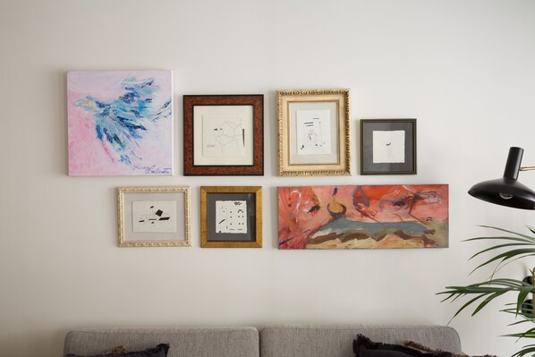 A wall with eight framed artworks of various styles and sizes.