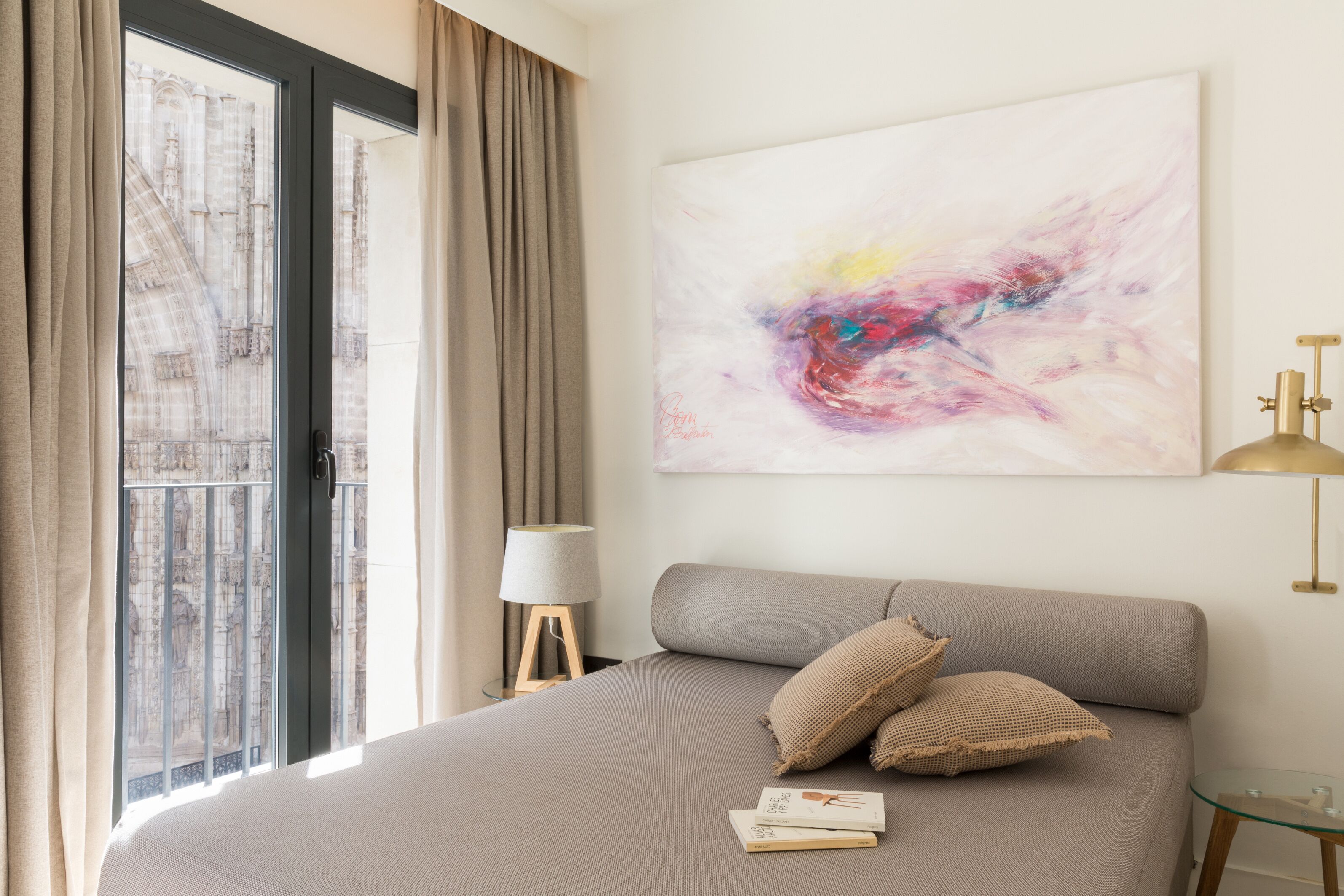 Une chambre avec un grand lit, une fenêtre avec des rideaux, une table de chevet avec une lampe et un tableau au mur.