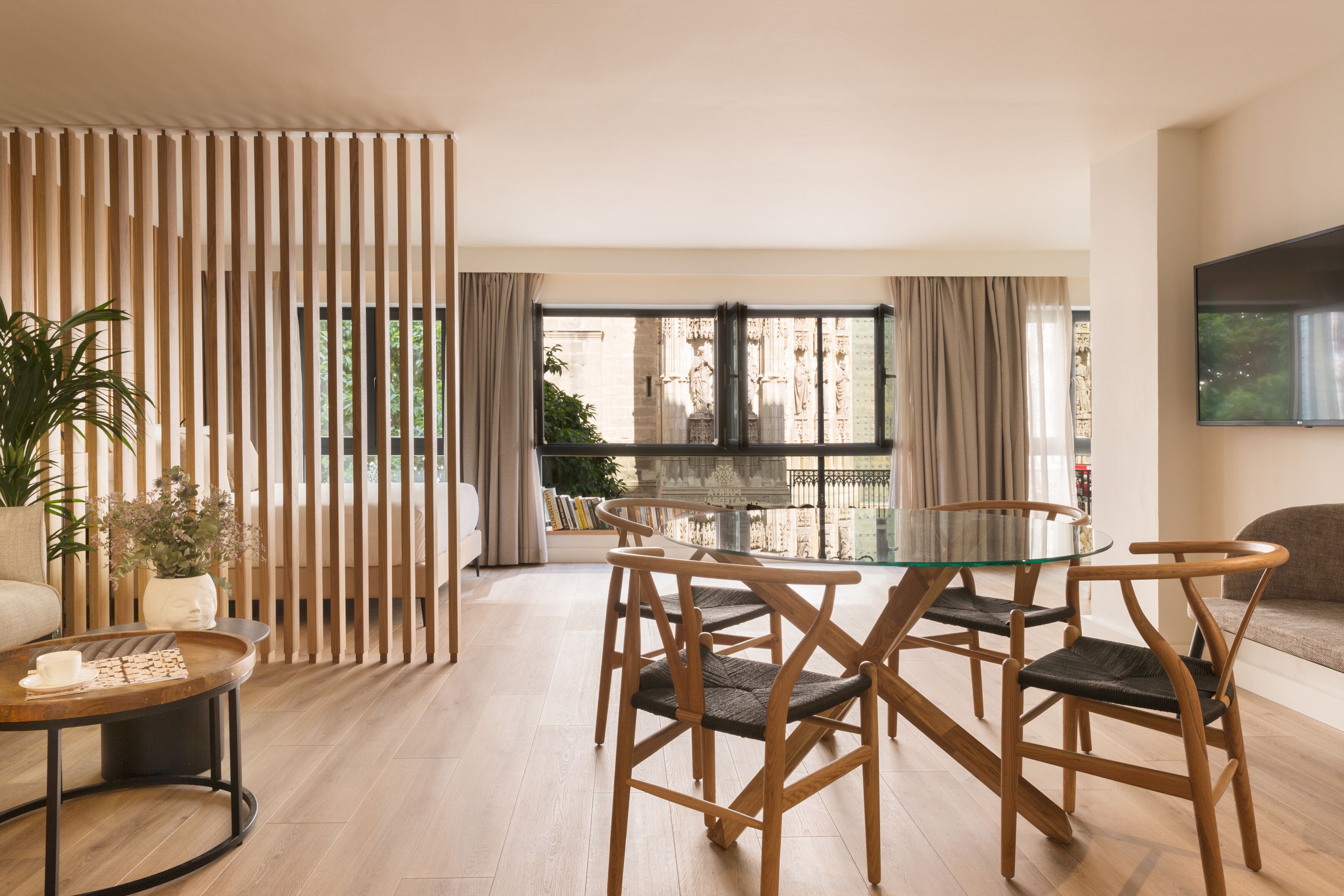 Un salon moderne avec une table à manger en verre, des chaises en bois, un canapé et un téléviseur fixé au mur.