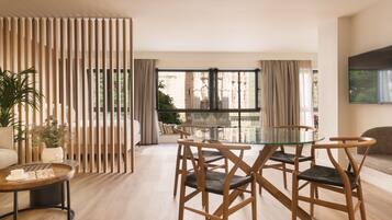 Un salon moderne avec une table à manger en verre, des chaises en bois, un canapé et un téléviseur fixé au mur.
