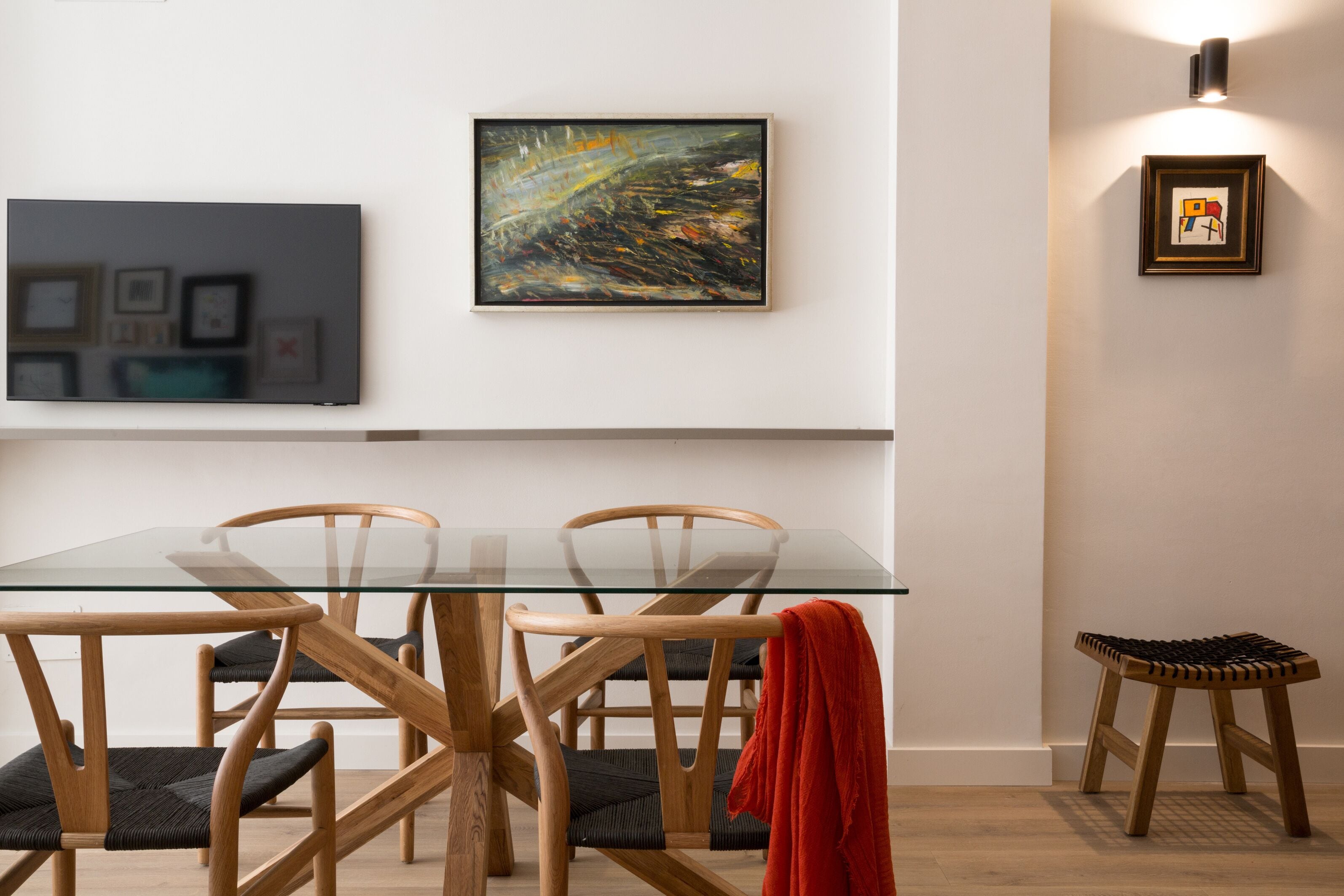 Un comedor con una mesa de vidrio, sillas de madera y un taburete pequeño.