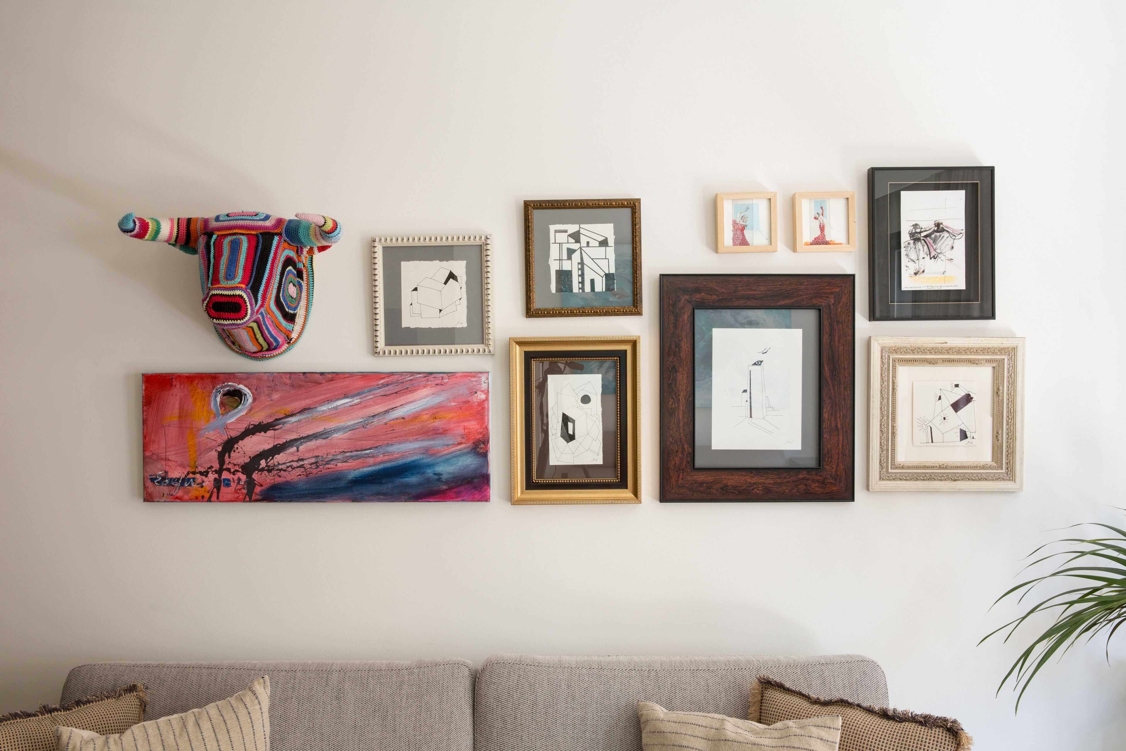 A wall with various framed artworks and a colorful bull head sculpture.