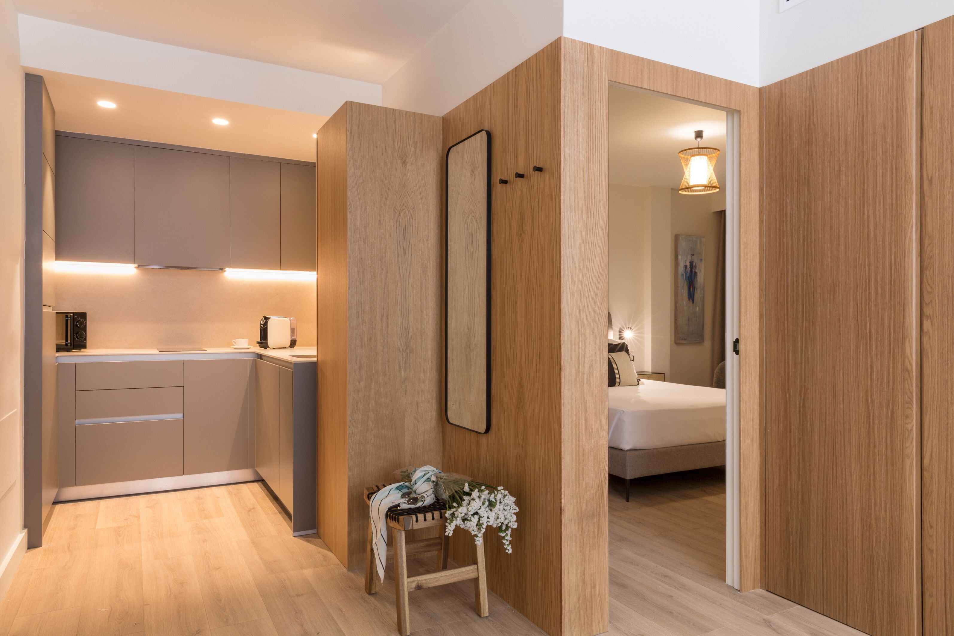Una cocina moderna con electrodomésticos integrados, un muro decorativo de madera y una pequeña zona de estar con una planta.