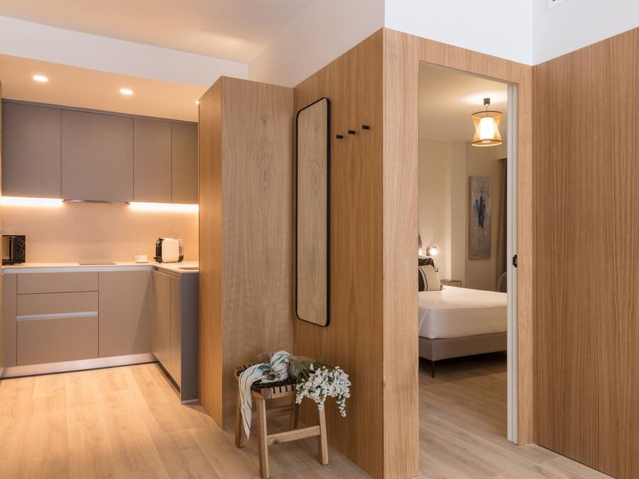 Una cocina moderna con electrodomésticos integrados, un muro decorativo de madera y una pequeña zona de estar con una planta.