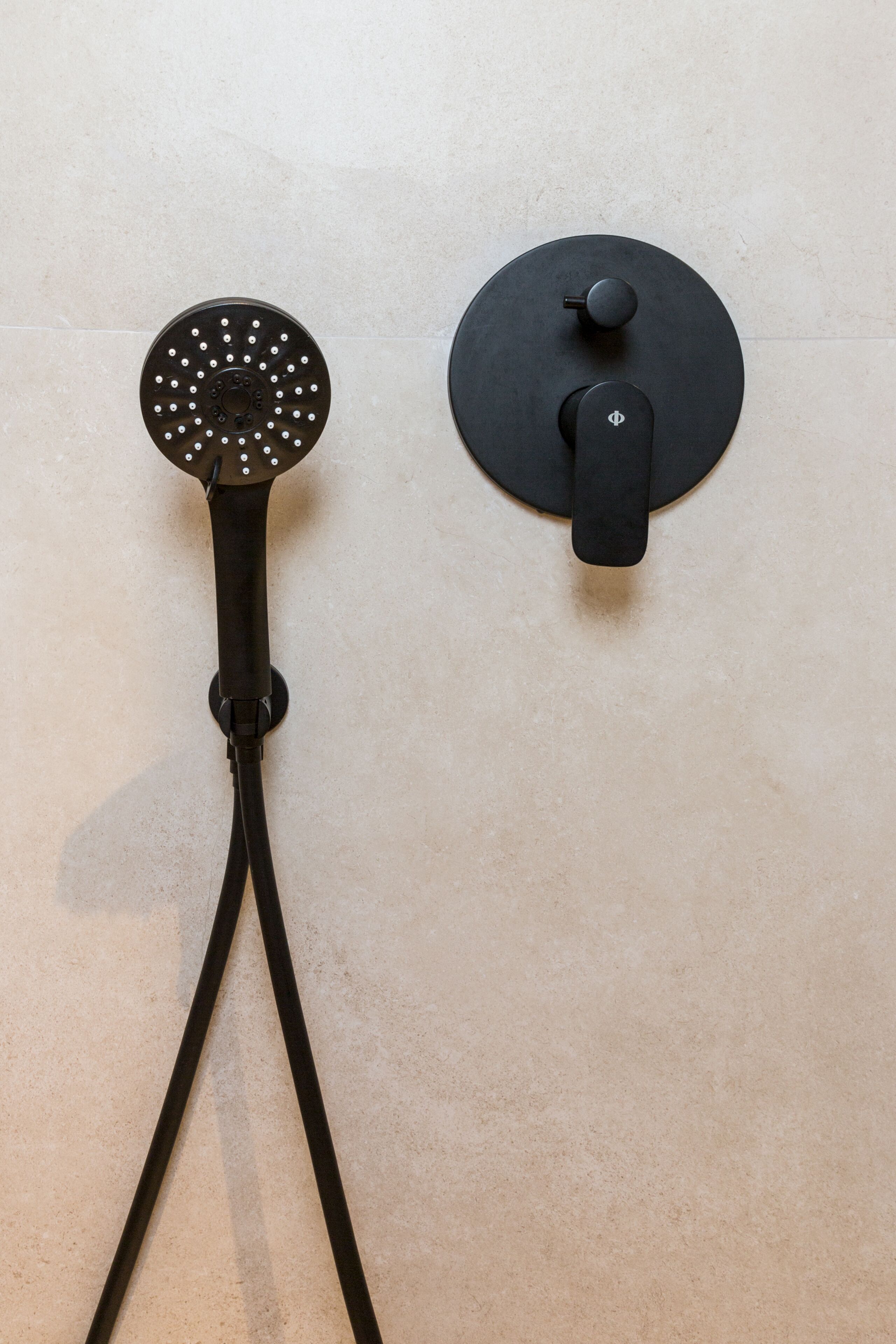 A shower with a circular head and a control knob on a tiled wall.
