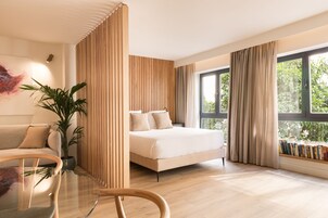 Un dormitorio moderno con una cama, una mesita de centro de vidrio, una planta en maceta y una estantería junto a la ventana.
