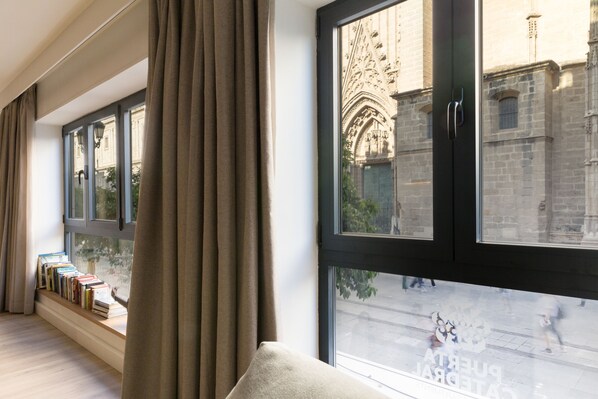 A room with a large window overlooking a historic building, a built-in bookshelf, and a cozy seating area.