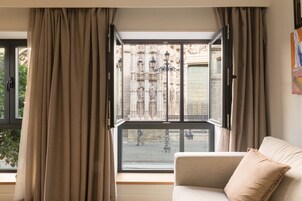 A room with a large window, a sofa, and a view of a street with a building in the background.