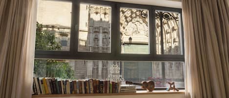 Een kamer met een groot raam, een boekenkast vol boeken en een gitaar.