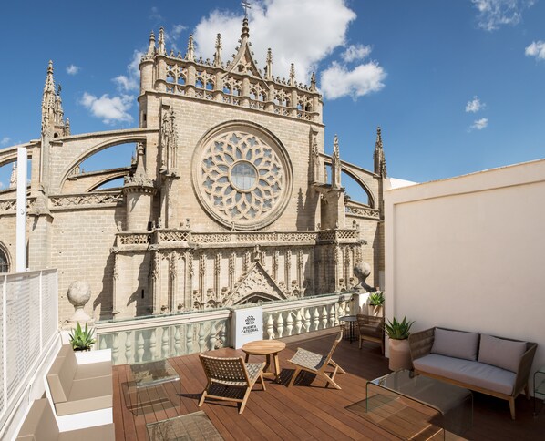 A rooftop terrace with a view of a historic cathedral, furnished with outdoor seating and potted plants. - Puerta Catedral Suites (Seville)