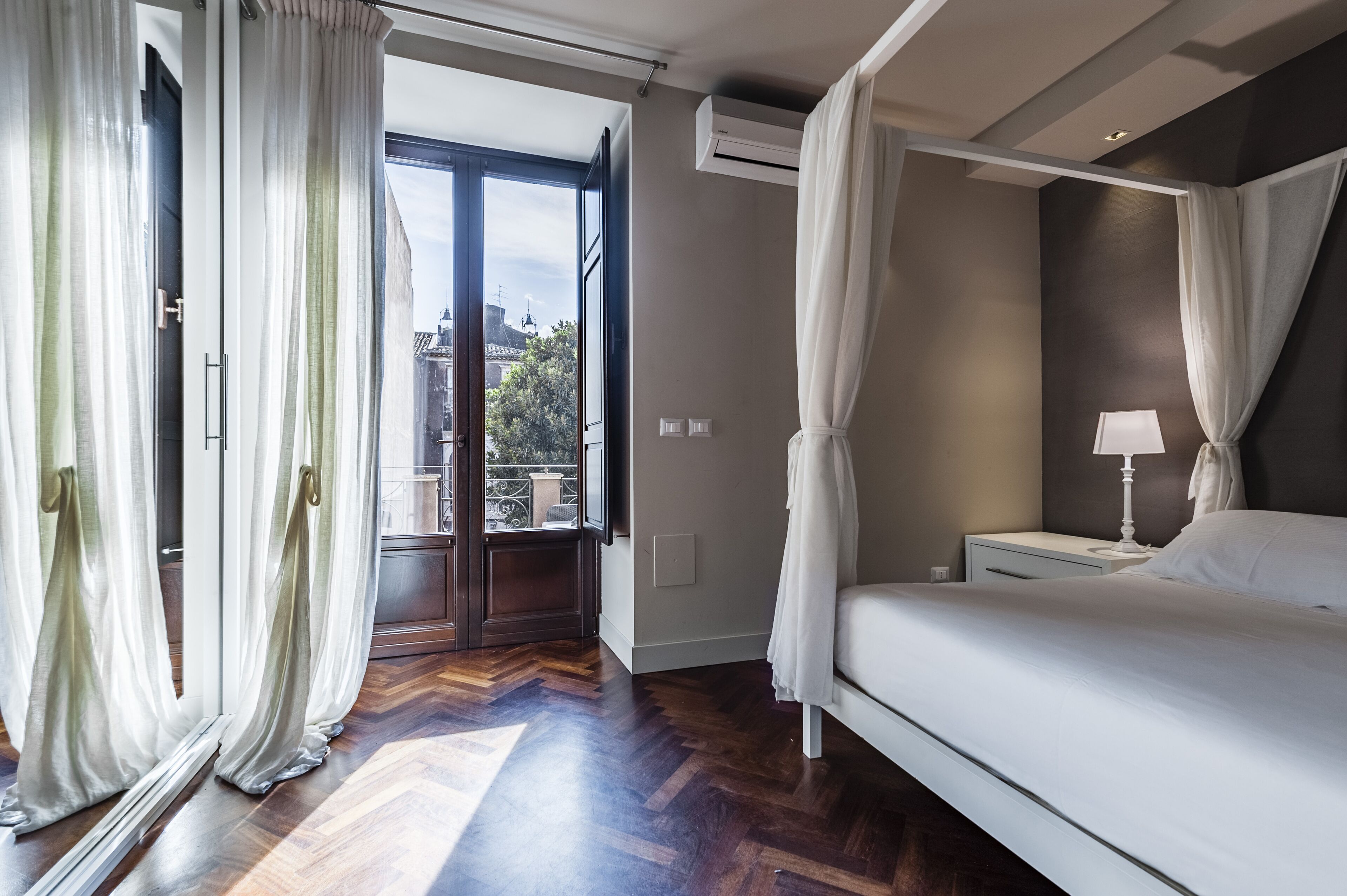 Une chambre à coucher avec un lit, une table de chevet, une lampe et une vue sur l’extérieur grâce à une grande fenêtre.