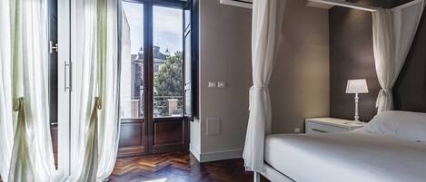 A bedroom with a bed, a nightstand, a lamp, and a view of the outdoors through a large window.