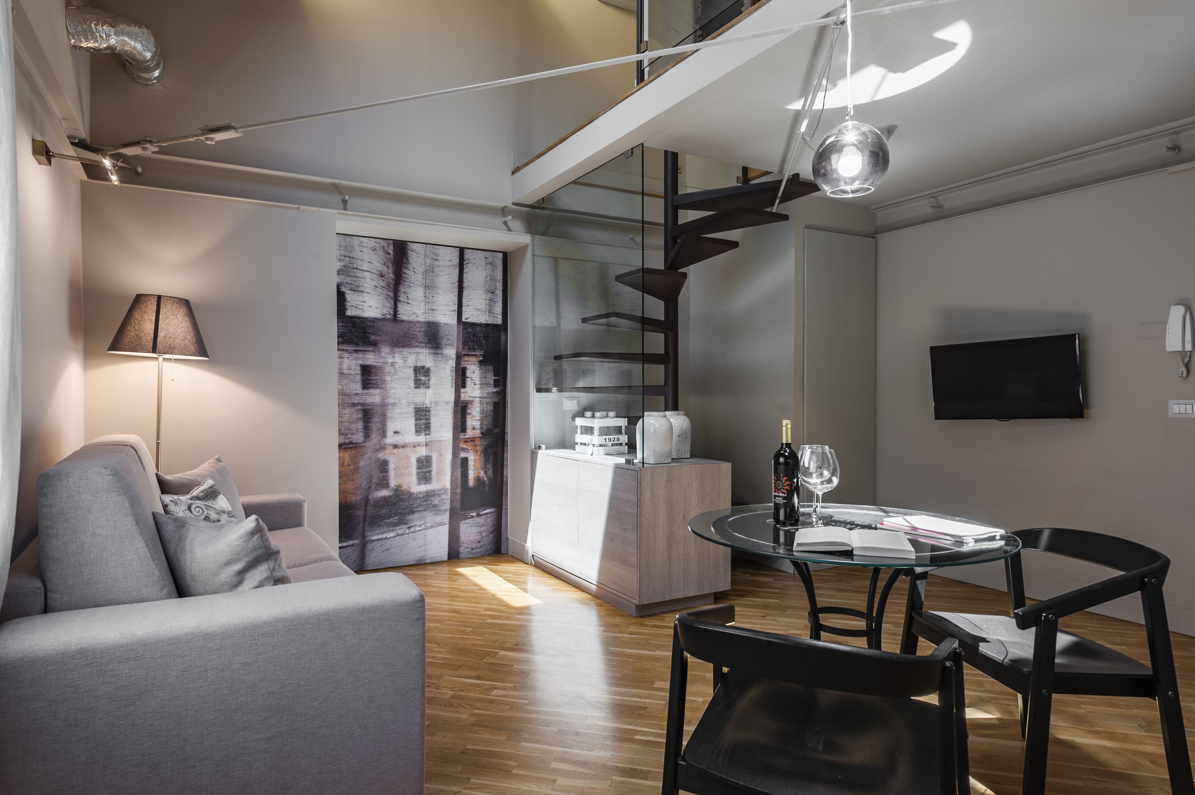 Een moderne woonkamer met een bank, een glazen eettafel en een aan de muur bevestigde televisie.