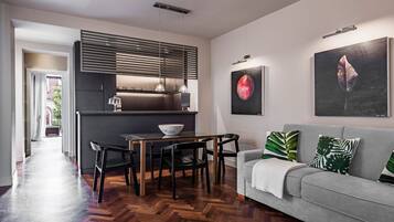 A modern kitchen with a dining area, a grey sofa with green cushions, and artwork on the walls.