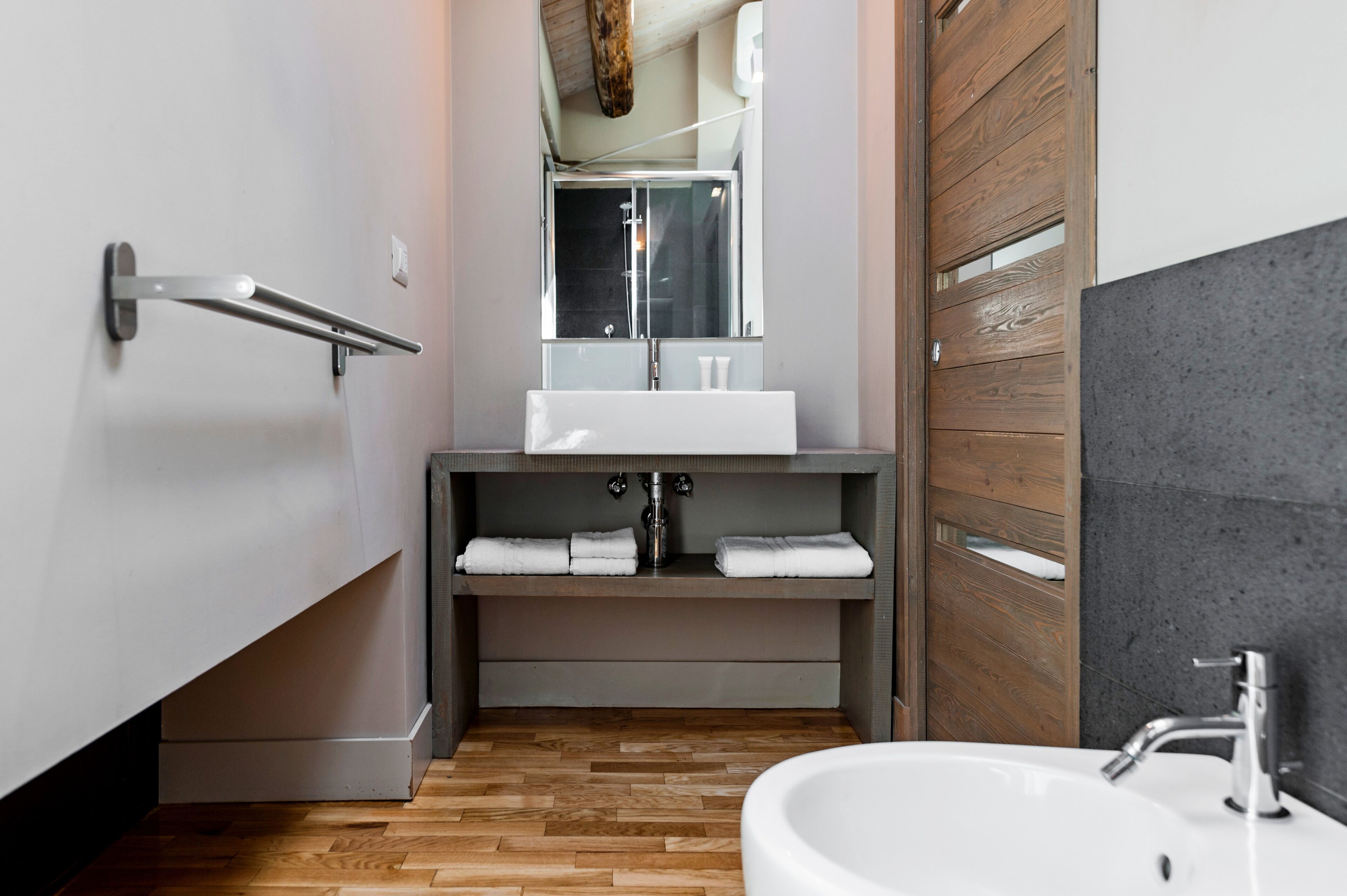 A modern bathroom with a wooden floor, a white sink, a mirror, and a towel rack.