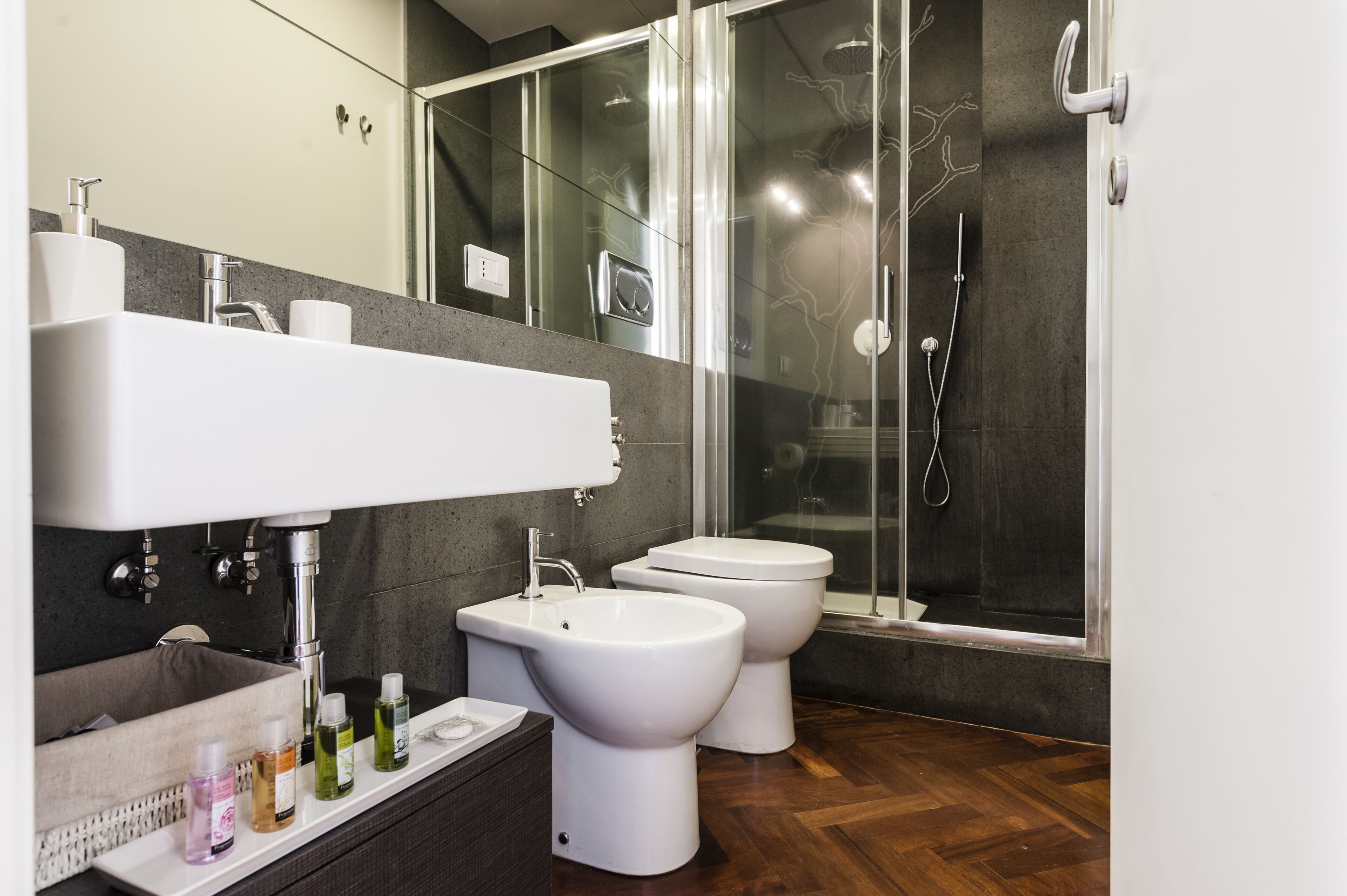 A modern bathroom with a glass-enclosed shower, a large sink, two toilets, and a vanity with toiletries.