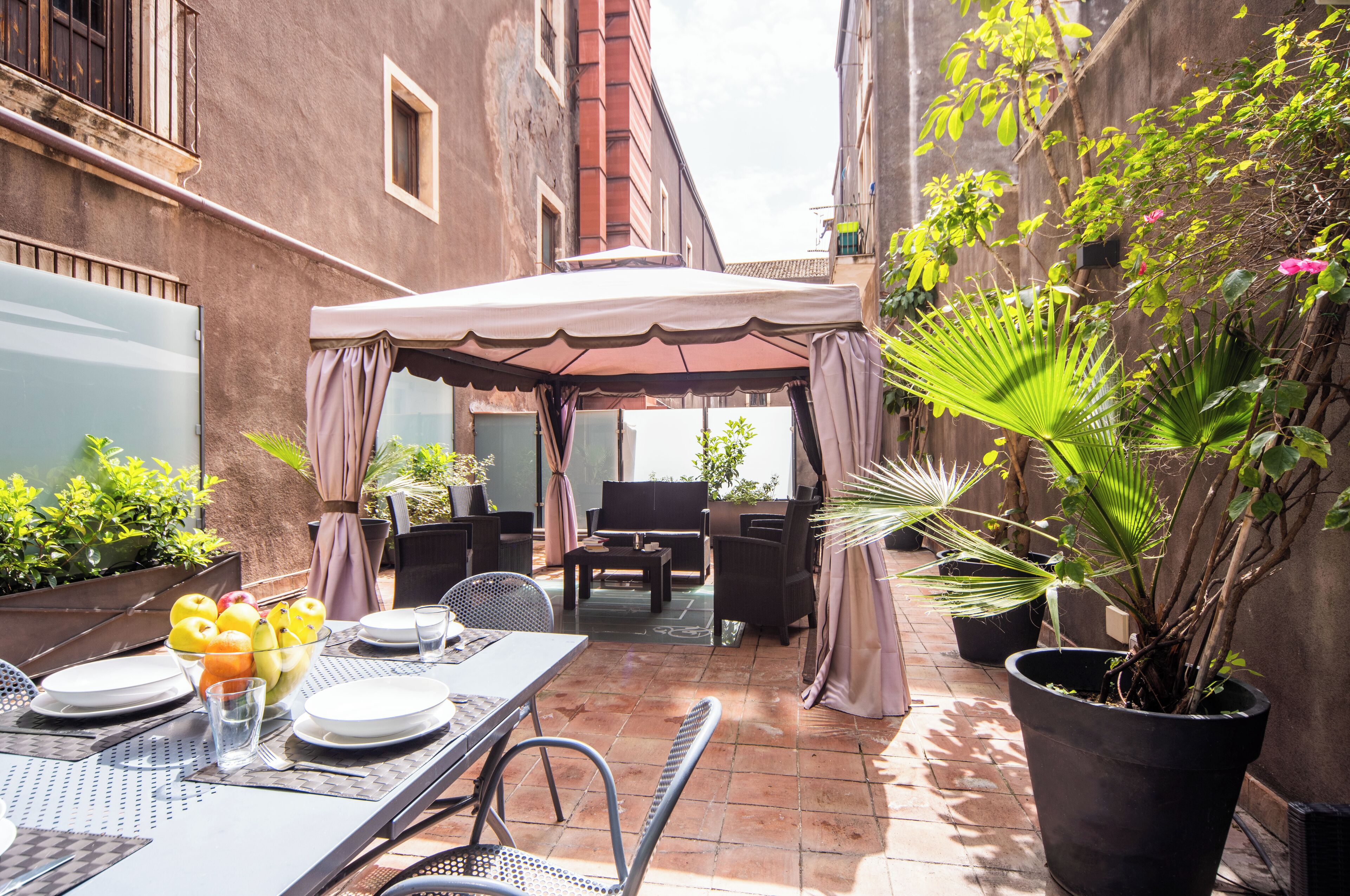 A patio area with a table set for dining, outdoor furniture, and potted plants.