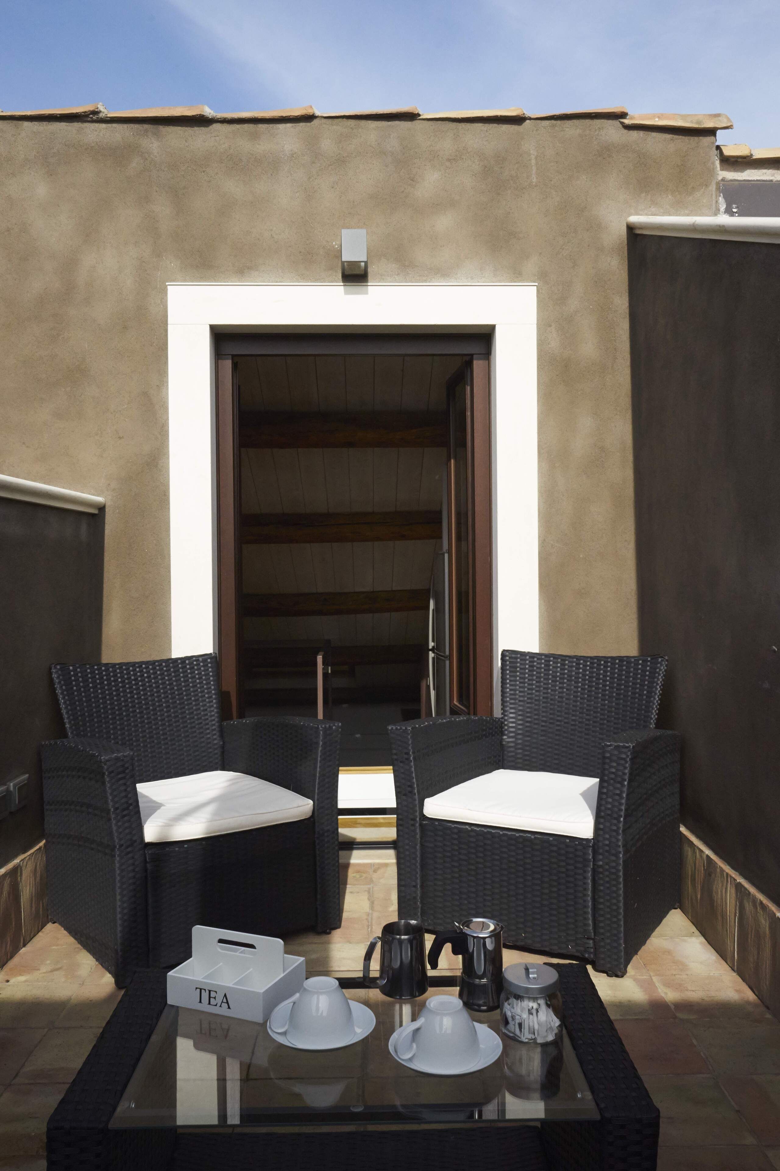A balcony with two wicker chairs, a glass table with tea set, and a door leading to an interior space.