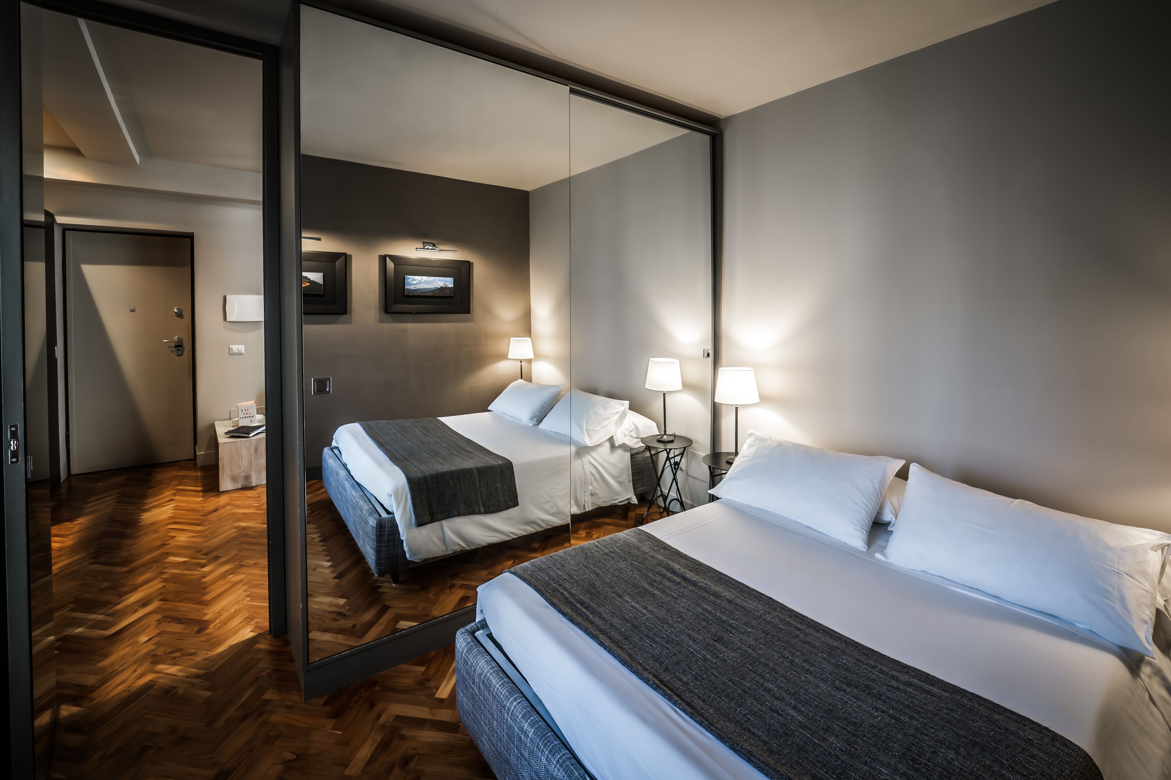 A hotel room with two beds, a large mirror, and a wooden herringbone floor.