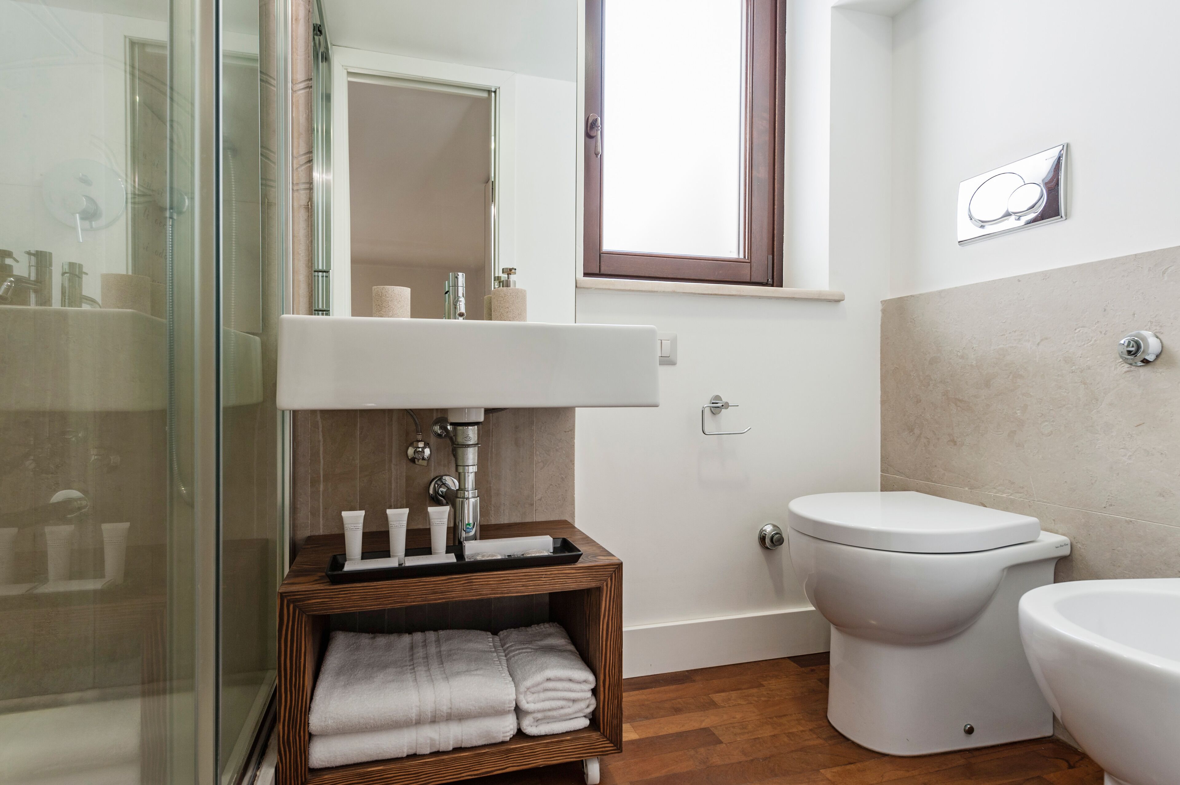Un bagno con box doccia in vetro, un mobile bagno in legno con lavandino e il water.