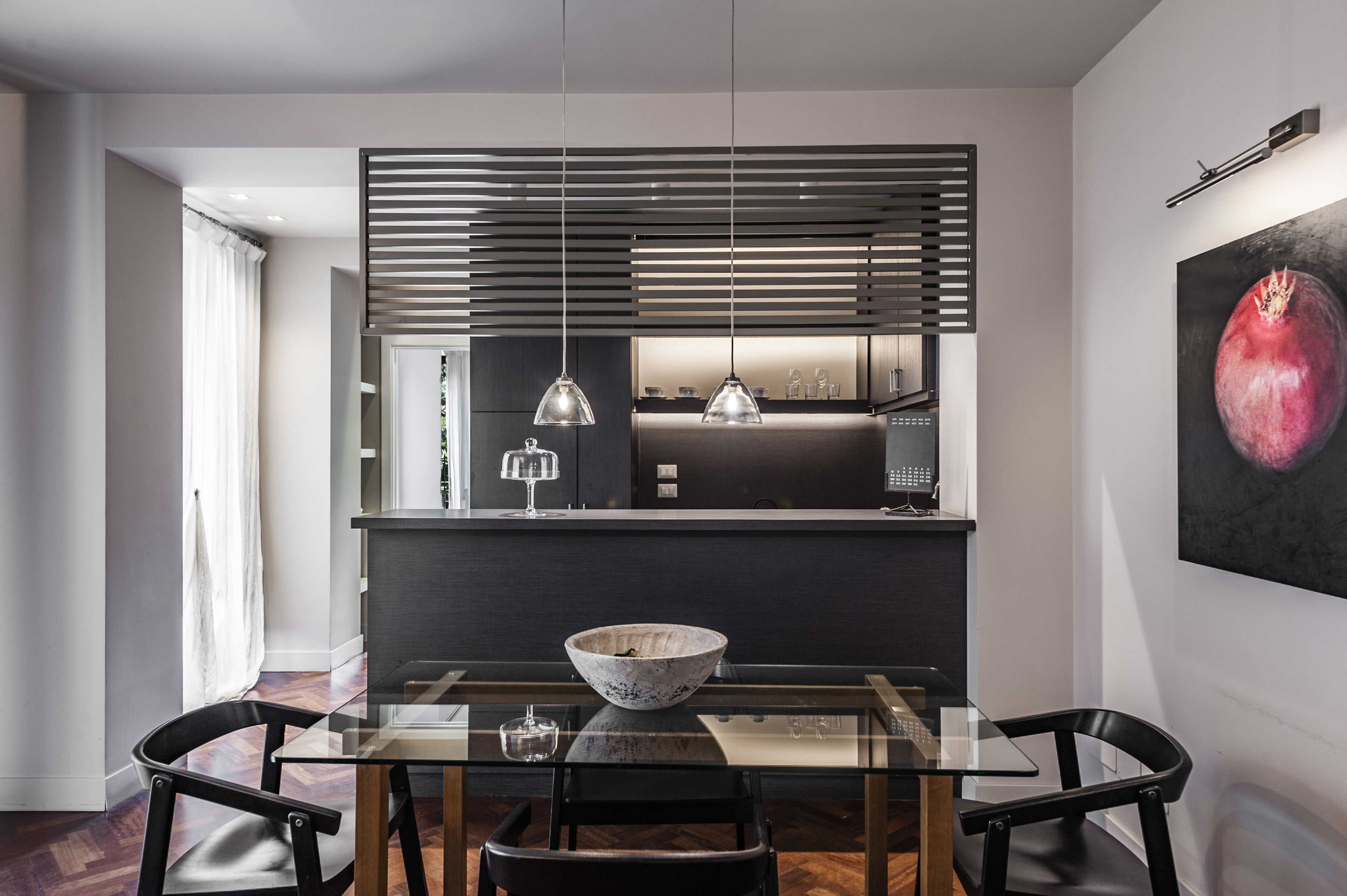 A modern dining area with a glass table, black chairs, a bowl, and pendant lights.