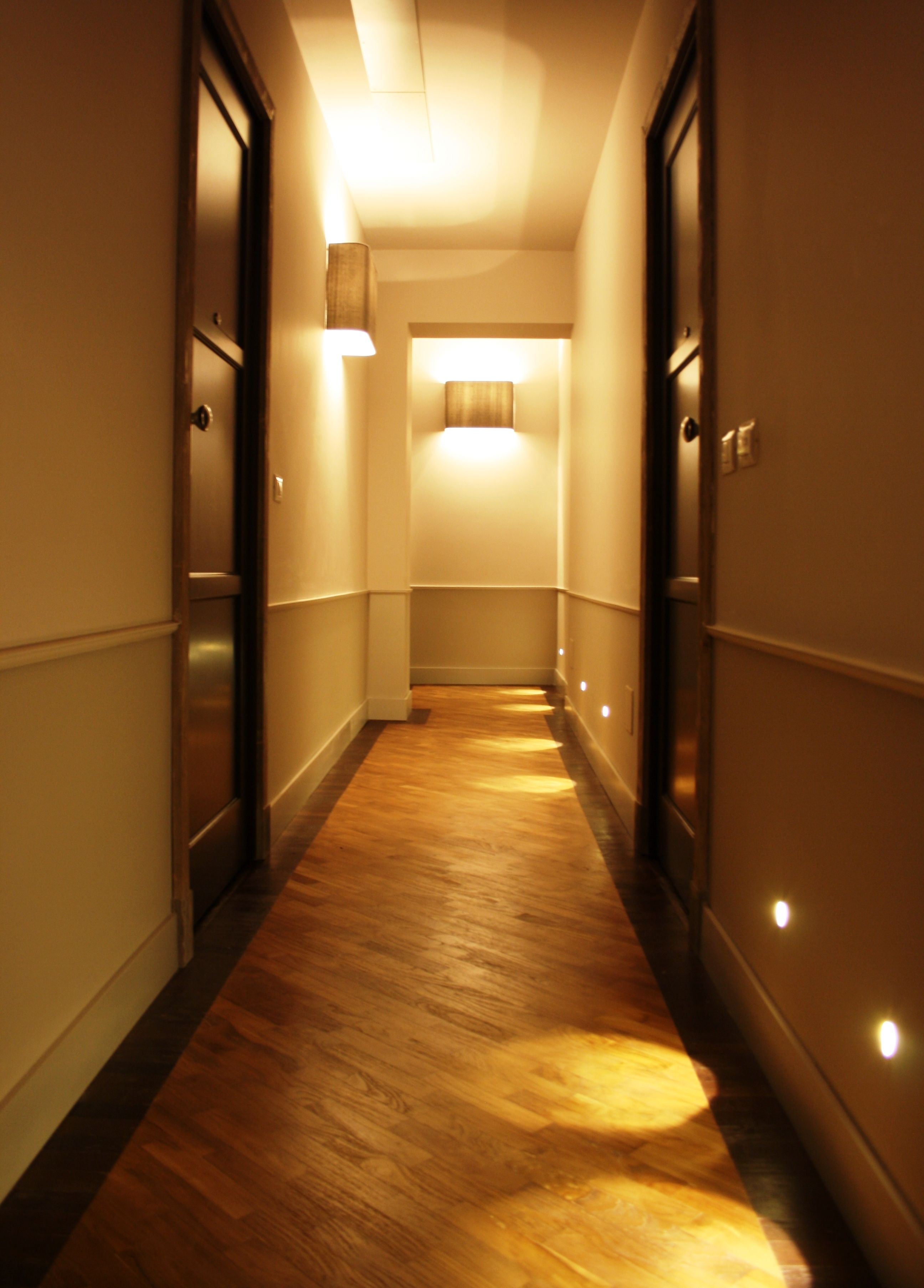 A narrow, well-lit hallway with wooden flooring and doors on both sides.