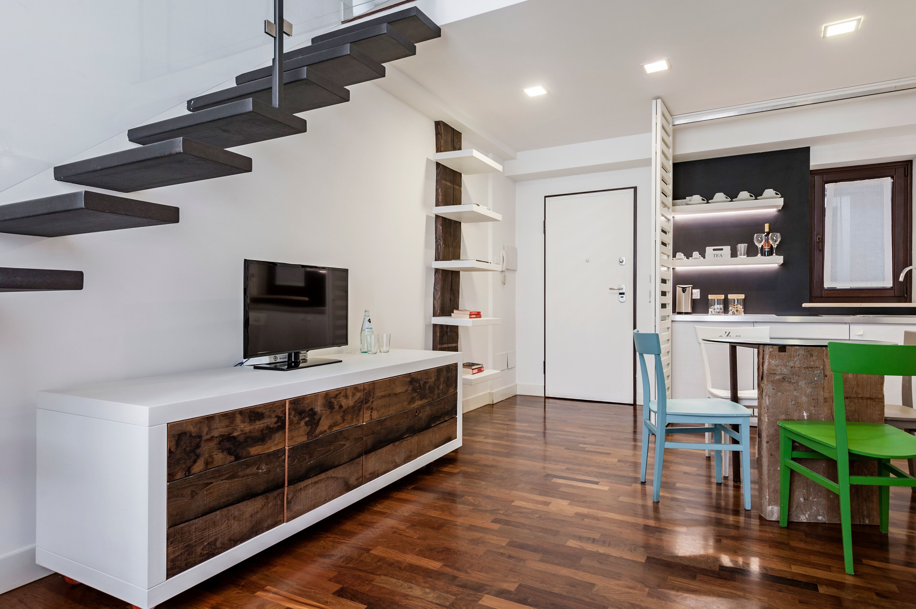 A modern kitchen with white cabinetry, a built-in stove, and a dining area with two chairs.