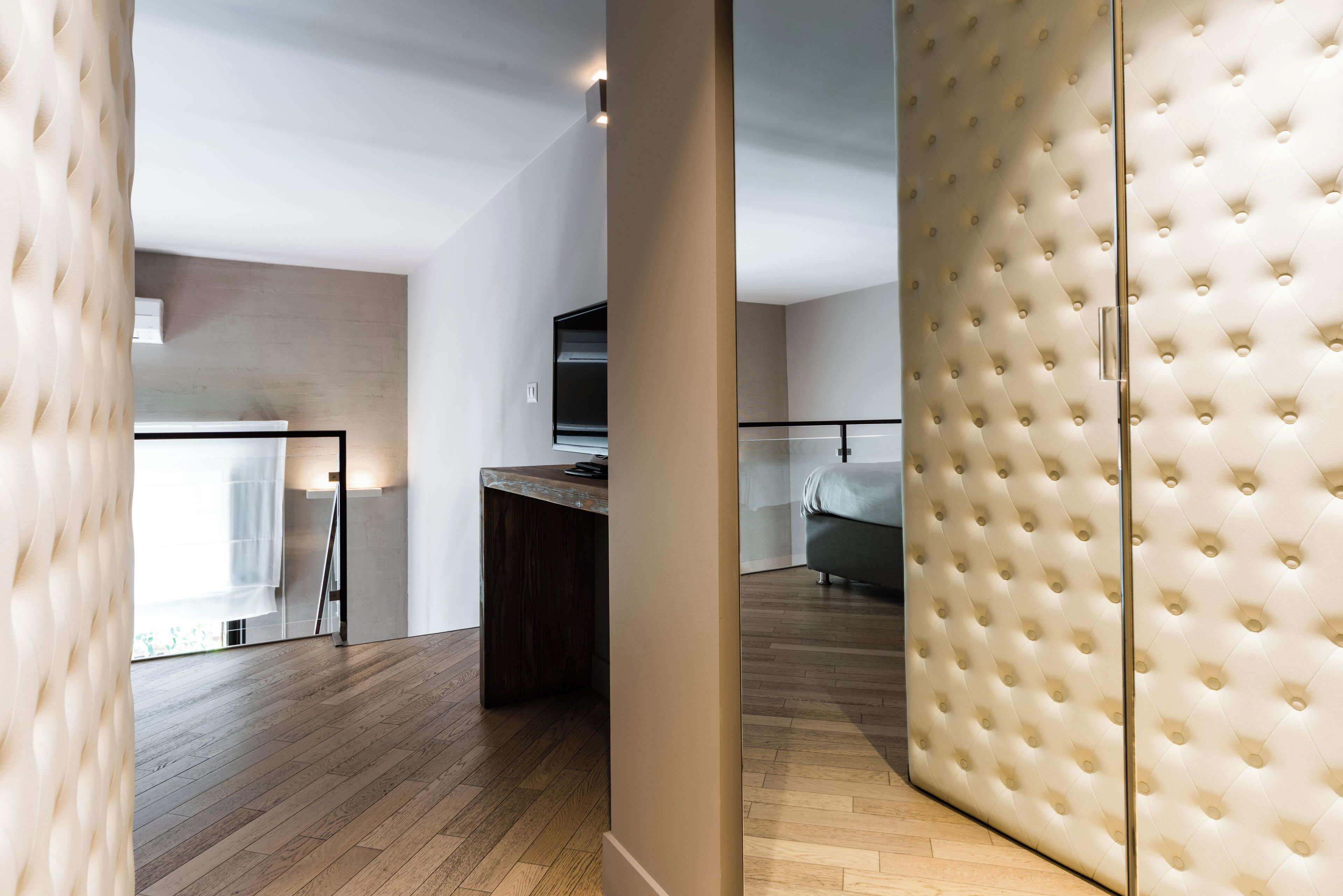 A modern interior with a wooden floor, a dark wooden desk, a grey sofa, and a tufted white partition.