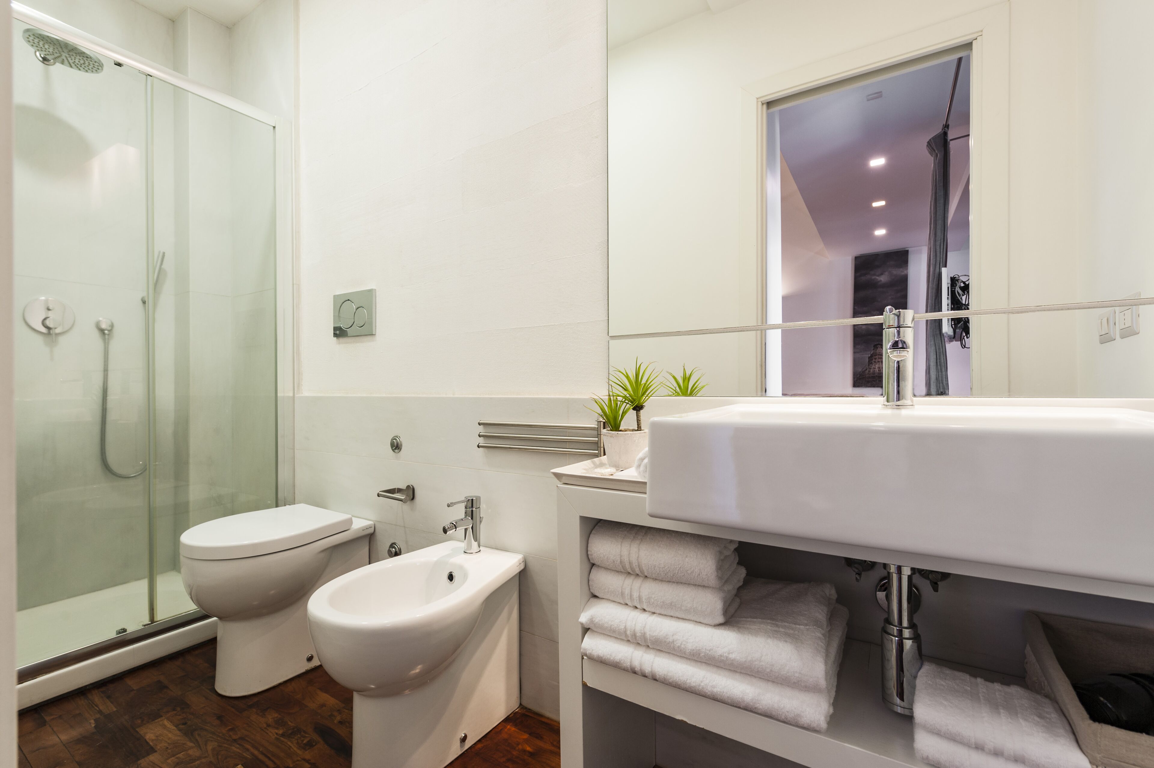 Un baño moderno con ducha de vidrio, inodoro, bidé y un lavamanos grande con un espejo arriba.