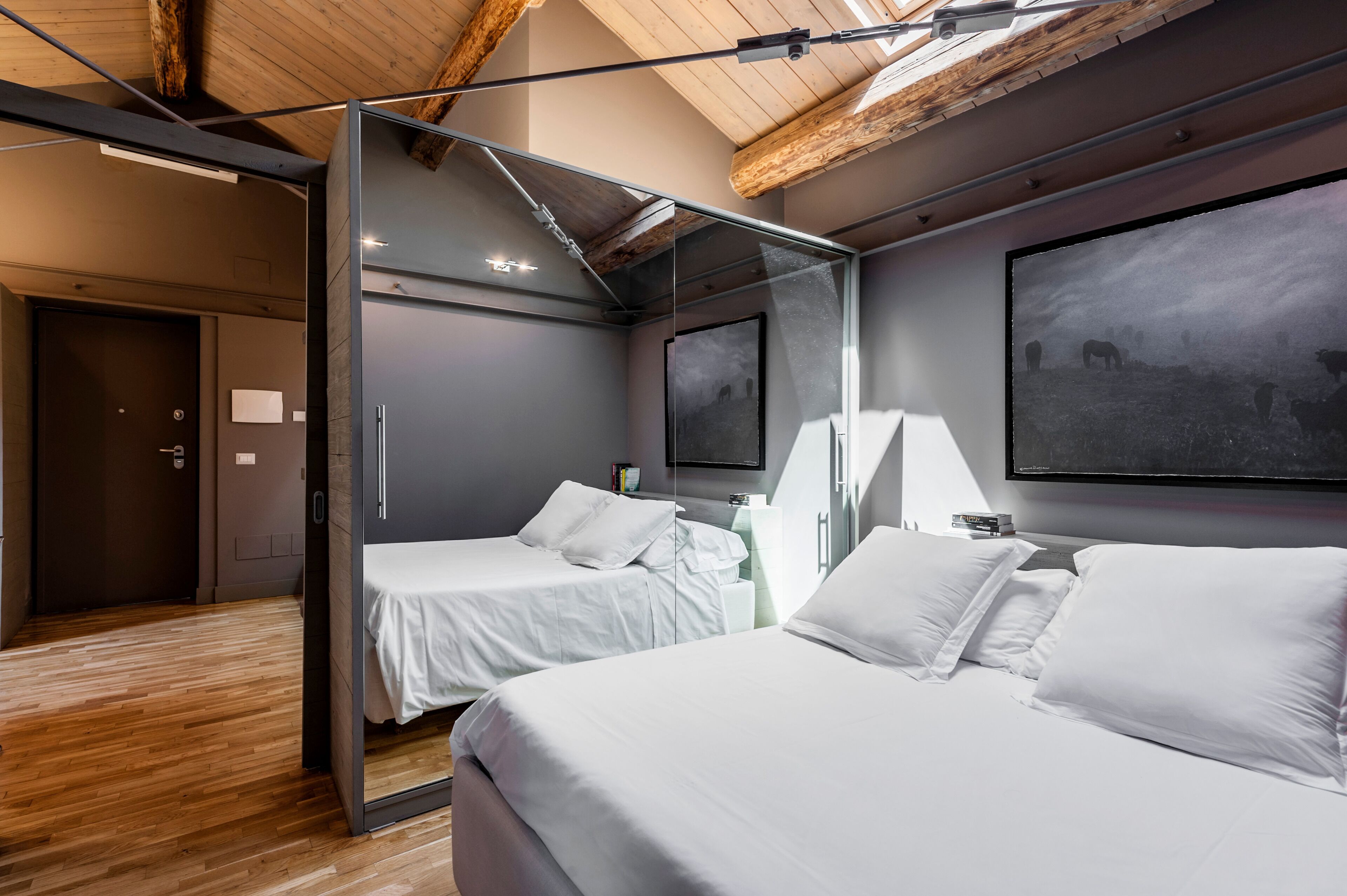 A modern hotel room with two beds, a large mirror, and a mounted TV.