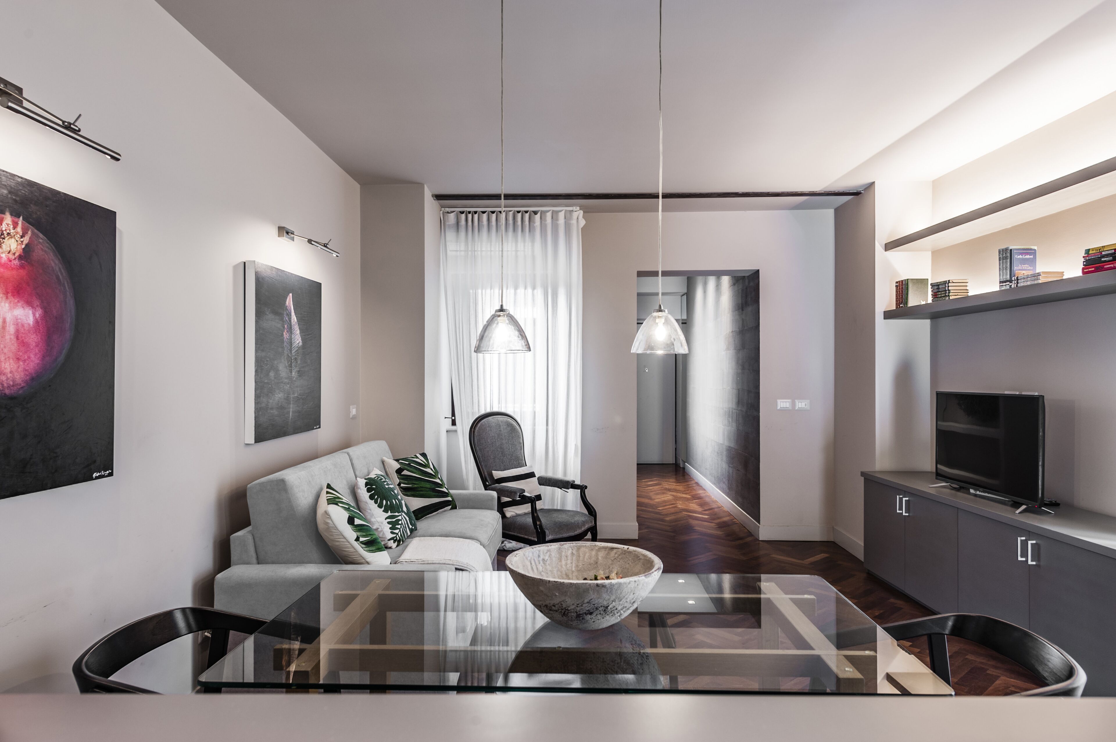 A modern living room with a glass coffee table, a grey sofa, and a dining area with a glass table.