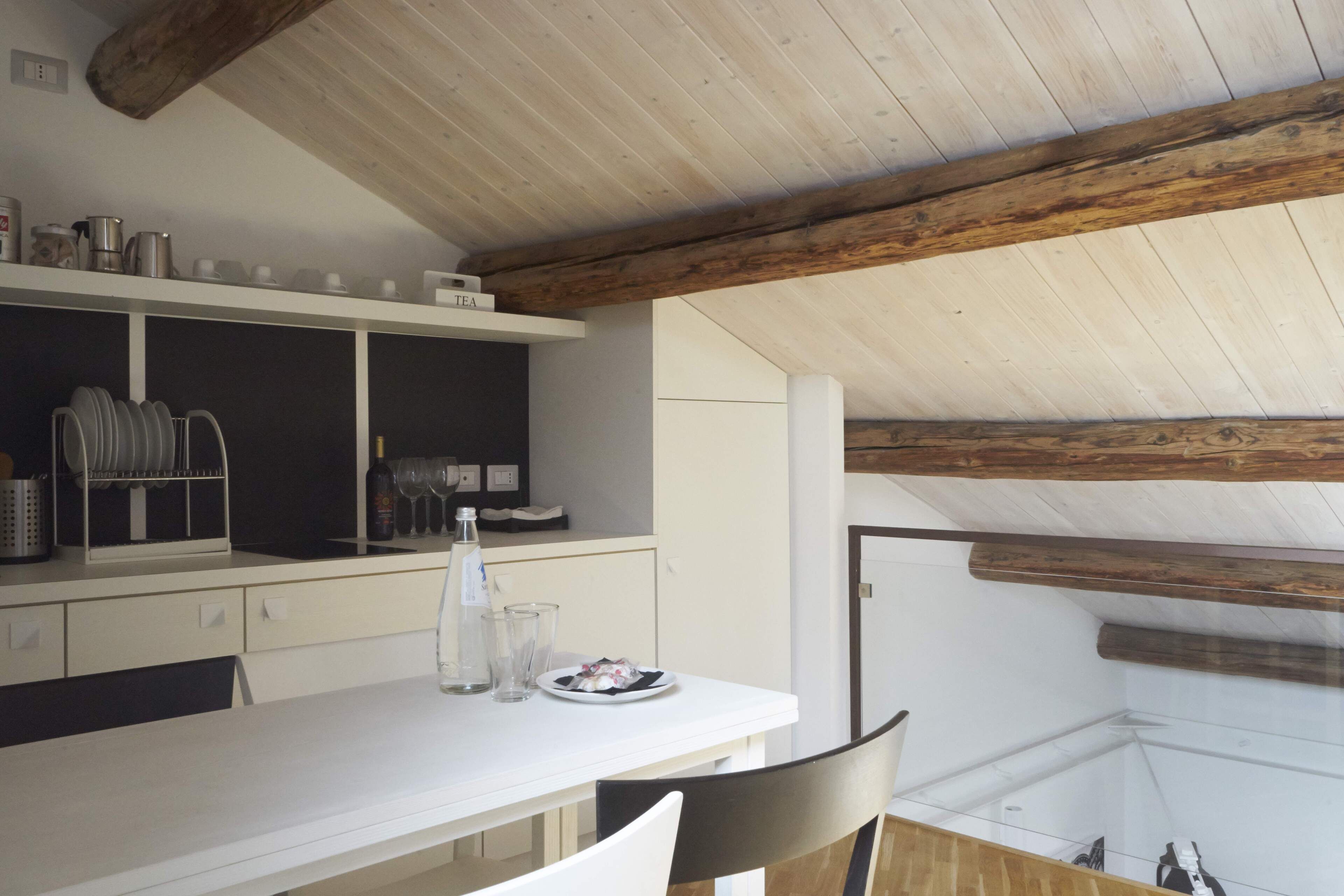 Eine moderne Küche mit weißen Schränken, einer Holzbalkendecke und einem Essbereich mit weißem Tisch und Stühlen.