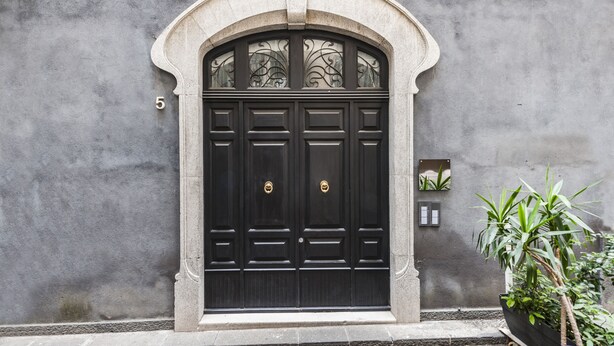 A black double door with a decorative arch above it, set in a concrete wall. - Ferrini Home - Via Monte Sant'Agata (Catania)