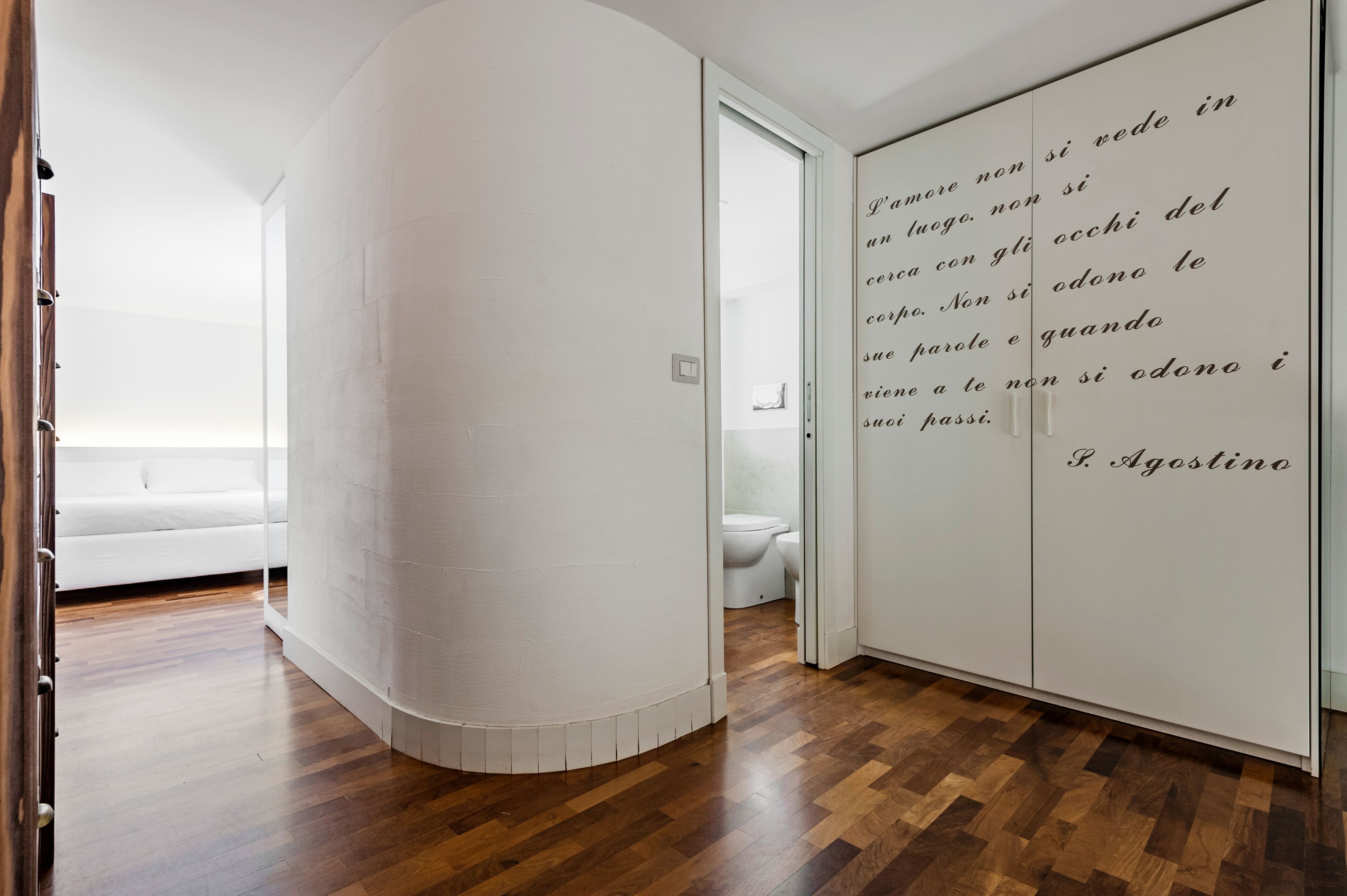 A modern room with a curved white wall, a wooden floor, and a white sofa.