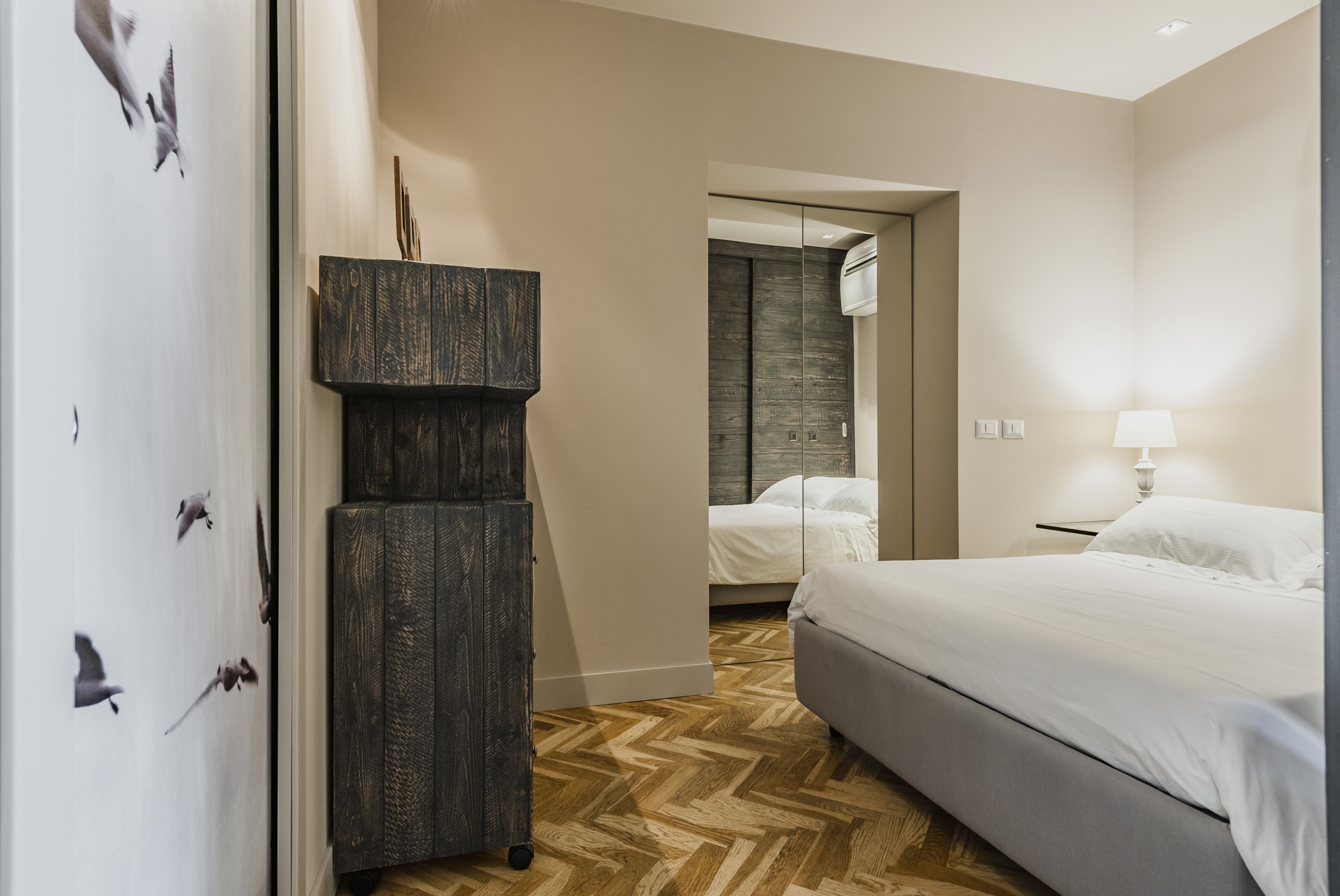 A hotel room with a bed, a wardrobe, a mirror, and a door leading to another room.