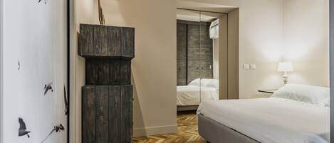 A hotel room with a bed, a wardrobe, a mirror, and a door leading to another room.