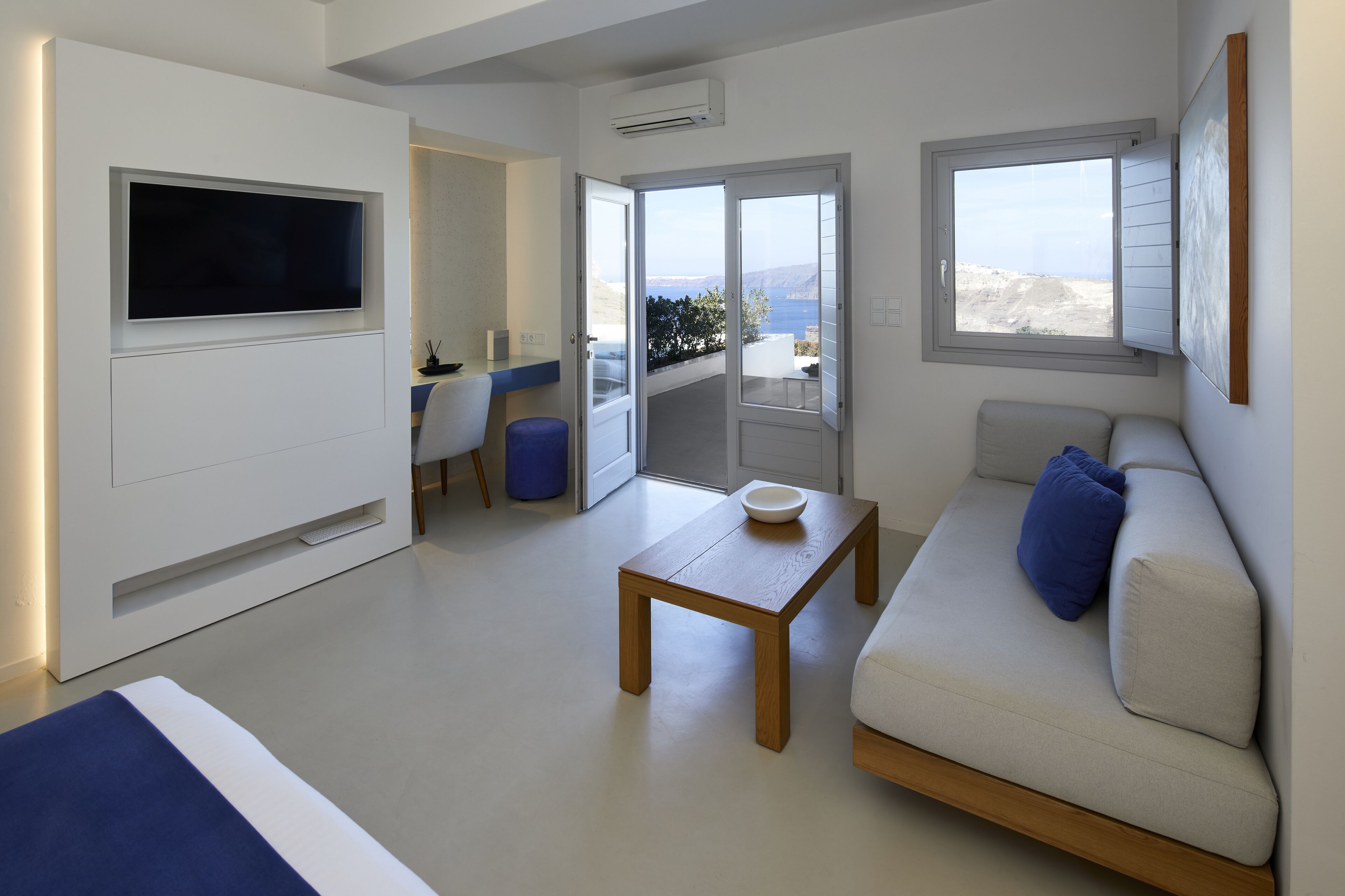 A modern living room with a flat-screen TV, a wooden coffee table, a sofa, and a balcony with a view.