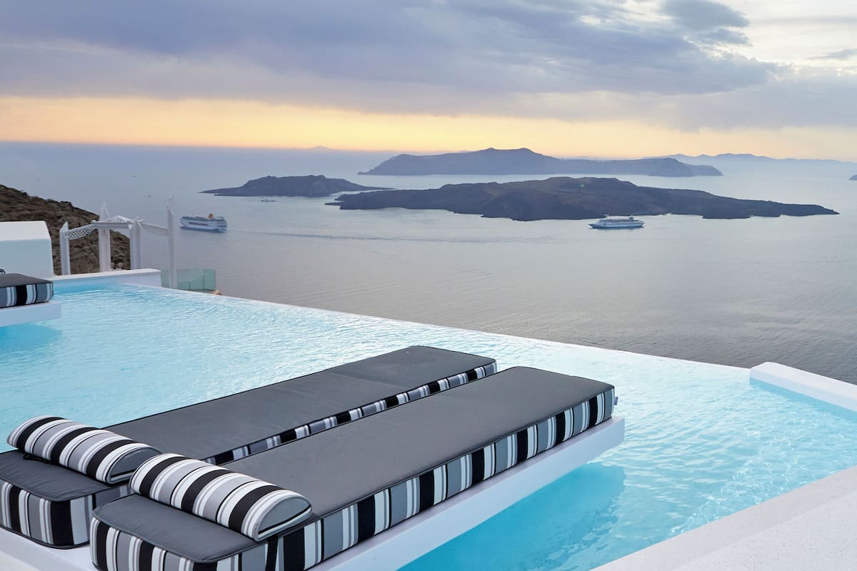 Una piscina infinita con tumbonas a rayas negras y blancas, vista al mar y un crucero en la distancia.
