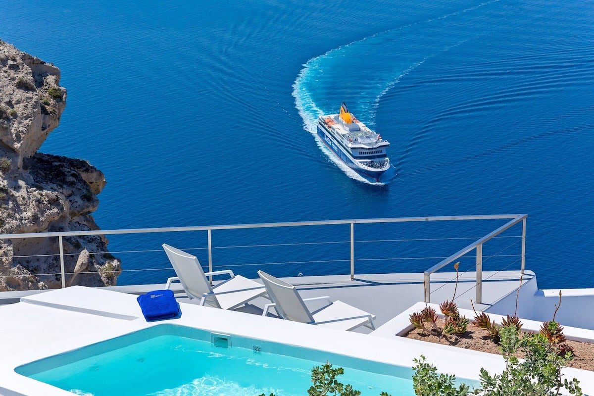 Zona de piscina con sillones, una piscina pequeña y vista al mar con un barco.