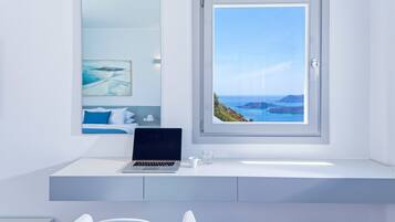 A modern bathroom with a laptop on the vanity, a large window with a coastal view, and a minimalist design.