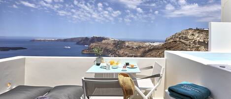 A balcony with a table set for breakfast, overlooking a coastal landscape with cliffs and the sea.