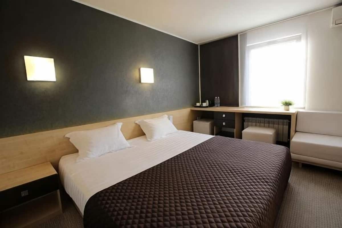Een hotelkamer met een bed, nachtkastjes, een bureau, een stoel en een raam.
