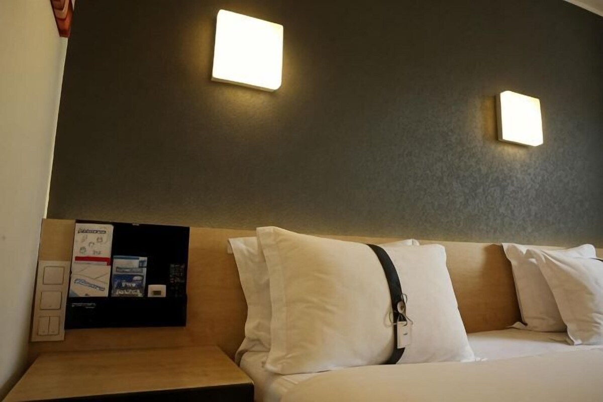 A hotel room with a bed, a nightstand, and two wall-mounted light fixtures.